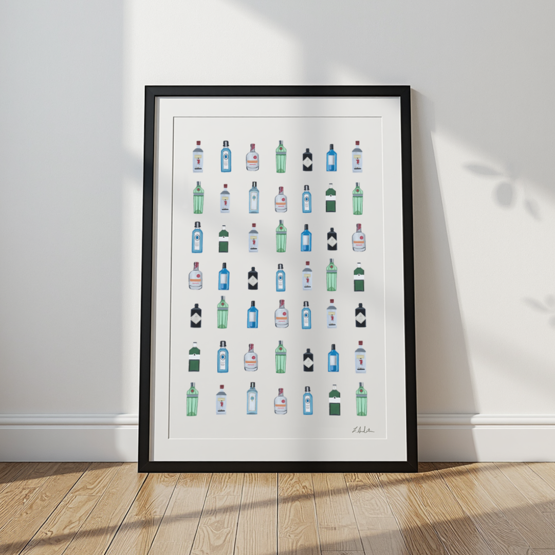 A framed art print featuring a grid of colorful illustrated liquor and spirit bottles, leaning against a white wall on a light wood floor.