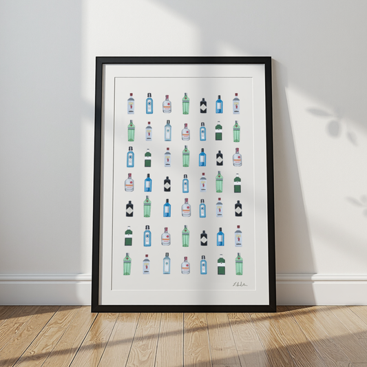 A framed art print featuring a grid of colorful illustrated liquor and spirit bottles, leaning against a white wall on a light wood floor.